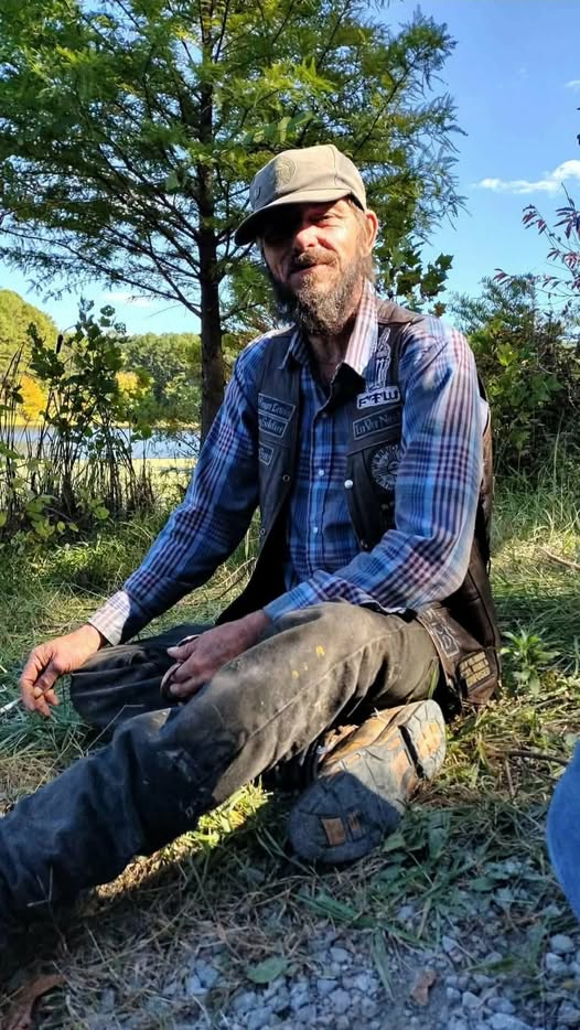 A loved one sitting outdoors by the water in a cap and vest